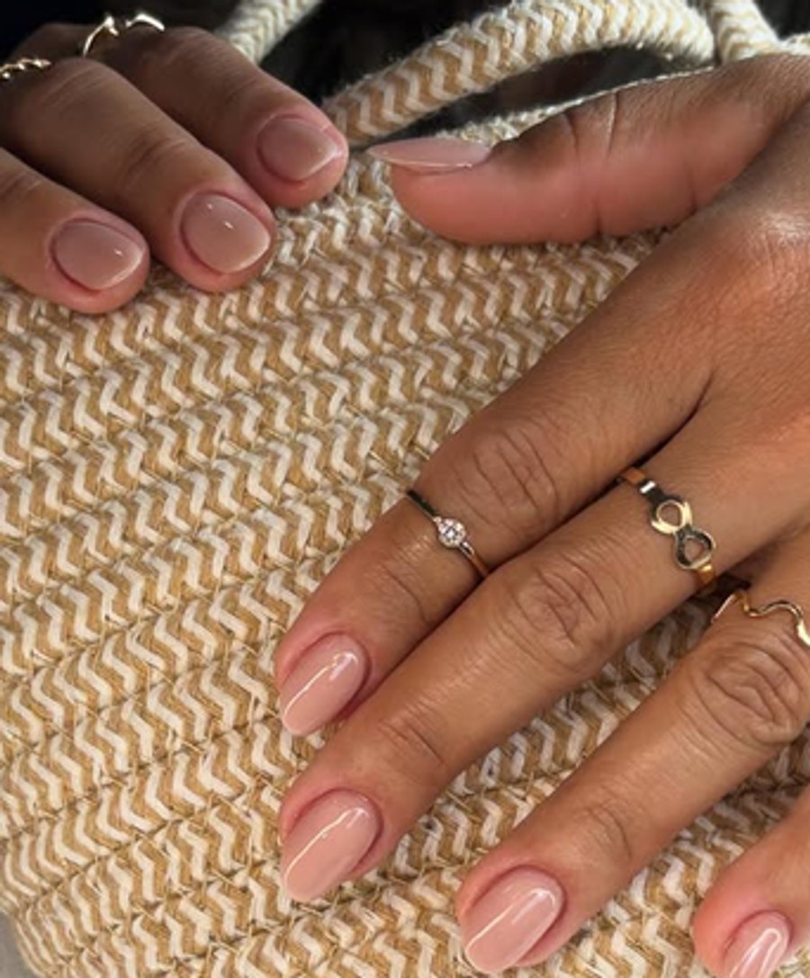 Unhas em gel tom nude natural sobre mala de palha